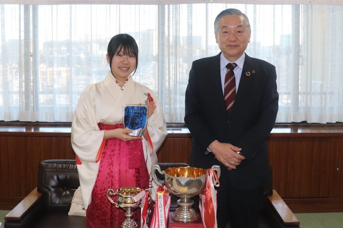 多摩市長特別賞の盾を手に市長と記念撮影する矢島さん